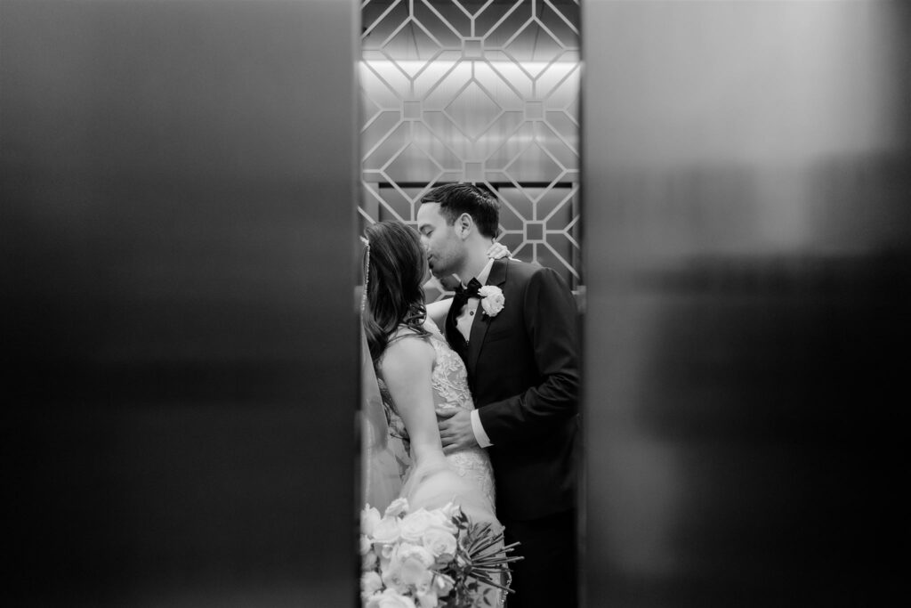 A black and white elevator photo of a bride and groom at the Loews Coral Gables wedding photographed by Angelika Krug Photo & Film a South Florida wedding photographer.